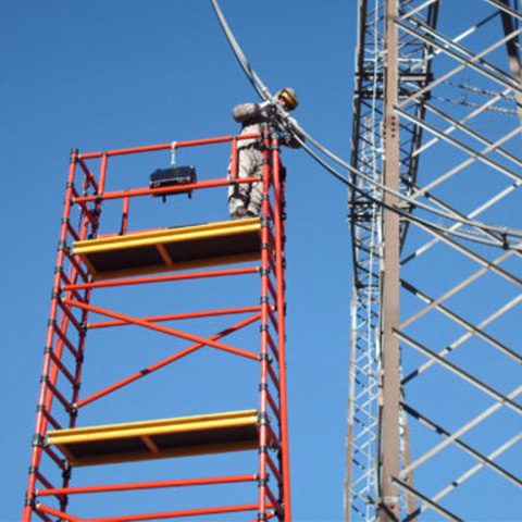 Construction worker on scaffold near metal tower against blue sky.
